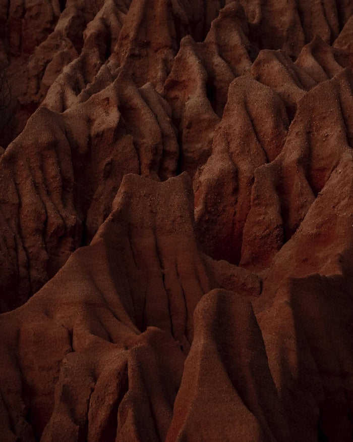 Dramatic red-brown rock formations with deep crevices and jagged spires creating an intricate canyon landscape