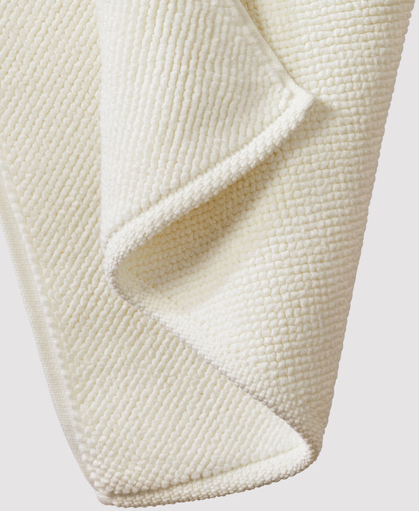 Cream-colored textured bath mat with raised dotted pattern, shown folded to display soft waffle-weave fabric detail