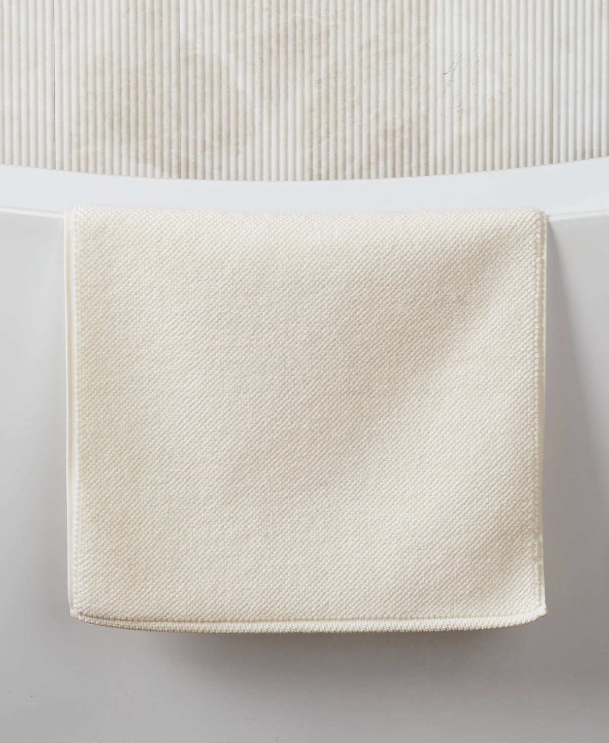 Cream-colored textured bath mat with woven pattern against white surface and ribbed background