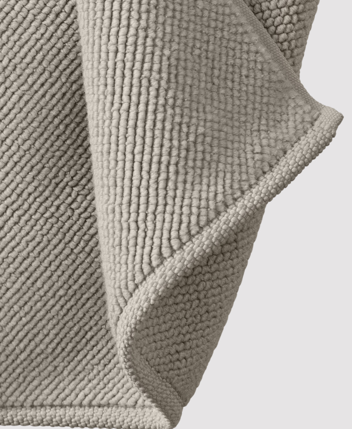 Textured beige bath mat with raised bobble pattern showing corner detail and soft fabric construction