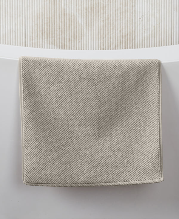 Beige textured bath mat with diagonal weave pattern displayed on white surface against ribbed background