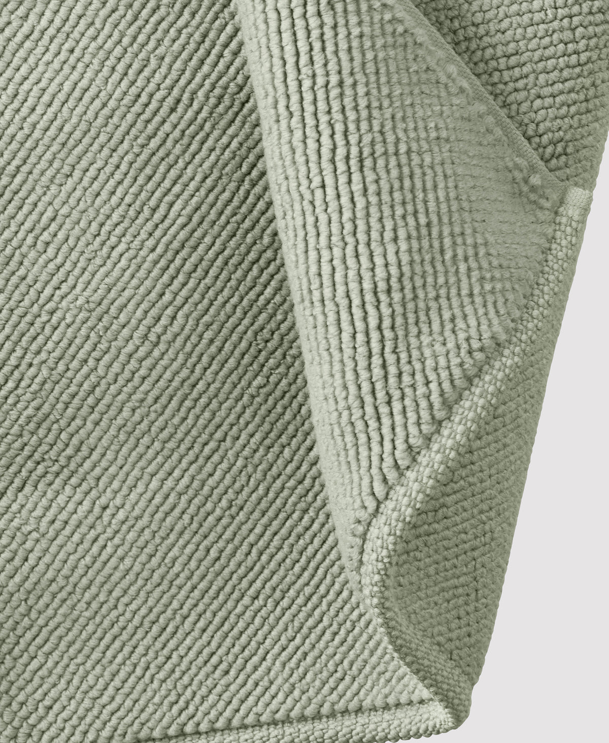 Sage green textured bath mat with raised geometric pattern and visible corner detail showing thick pile construction