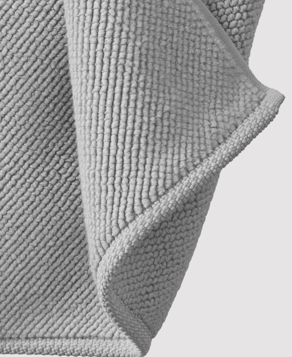 Gray textured bath mat with raised circular pattern and curved edges shown in detail against white background