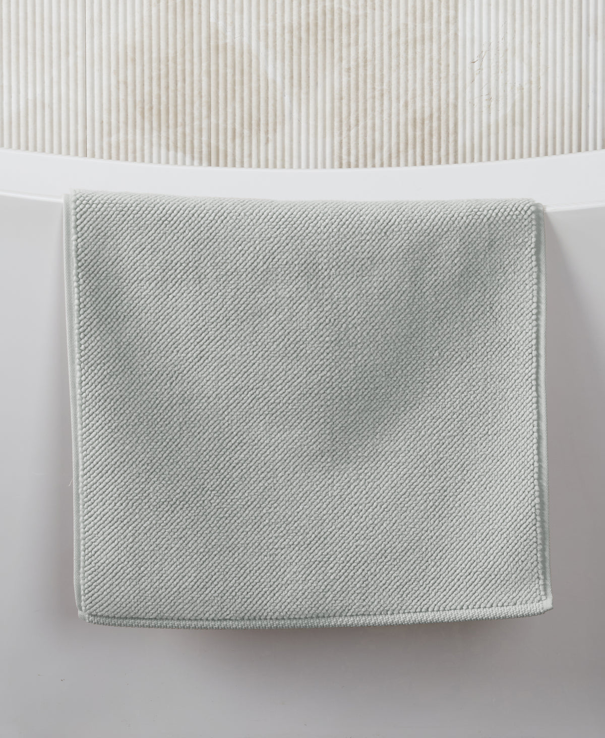 Gray textured bath mat with diagonal weave pattern displayed on white surface against ribbed white wall