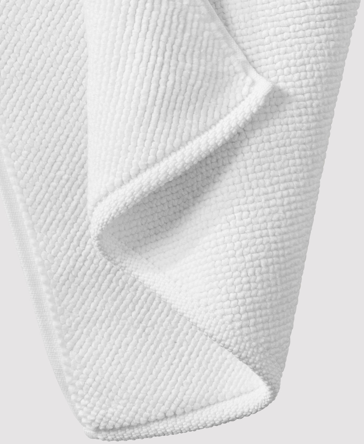White textured bath mat with waffle weave pattern, showing folded corner detail against white background