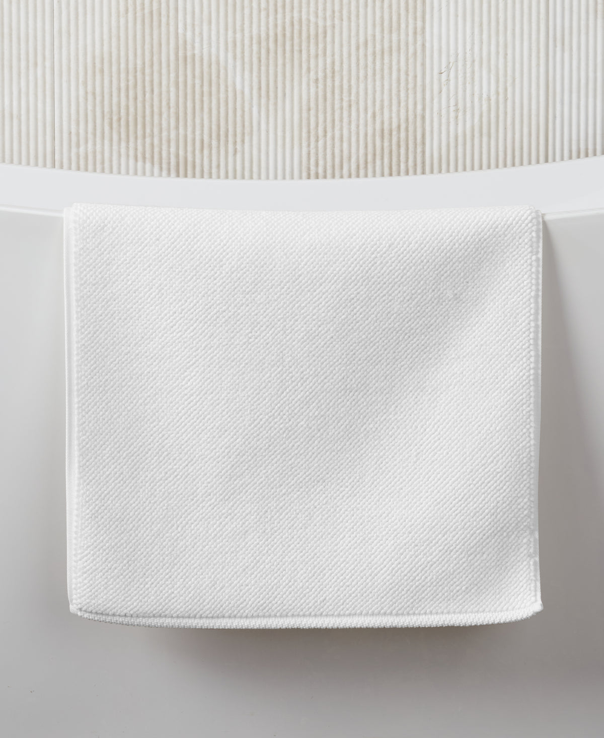 White textured bath mat hanging on white wall with beadboard wainscoting above