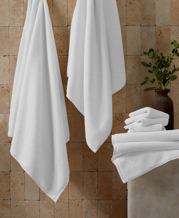 White ribbed towels hanging on hooks and folded in stack against textured stone wall with plant in vase