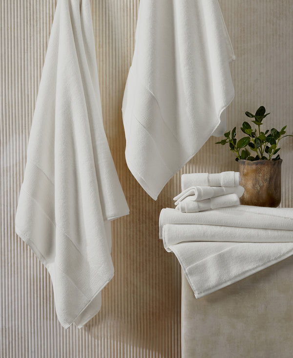 White towels hanging and stacked on neutral textured wall with small potted plant in bathroom setting
