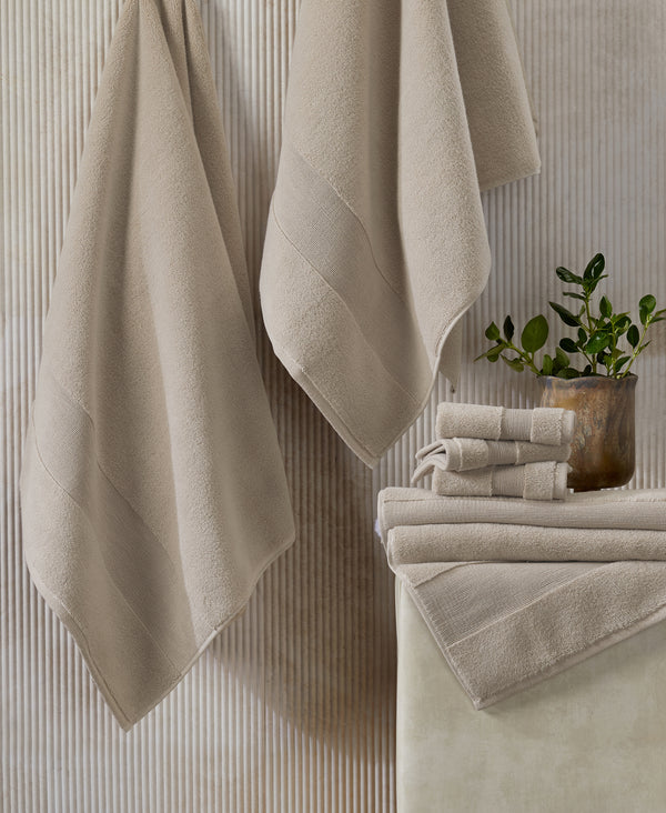 Beige towels hanging on hooks and stacked on white surface with small potted plant against textured wall