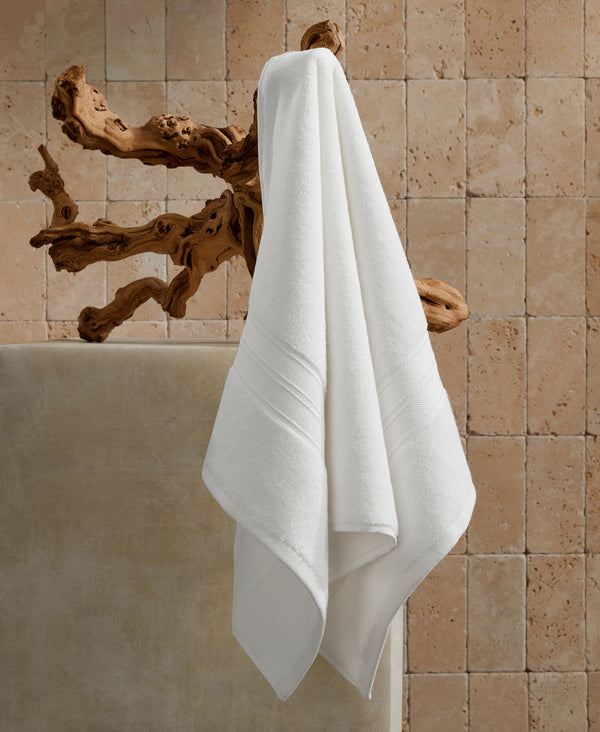 White towels hanging on driftwood hook mounted on beige stone tile bathroom wall next to bathtub