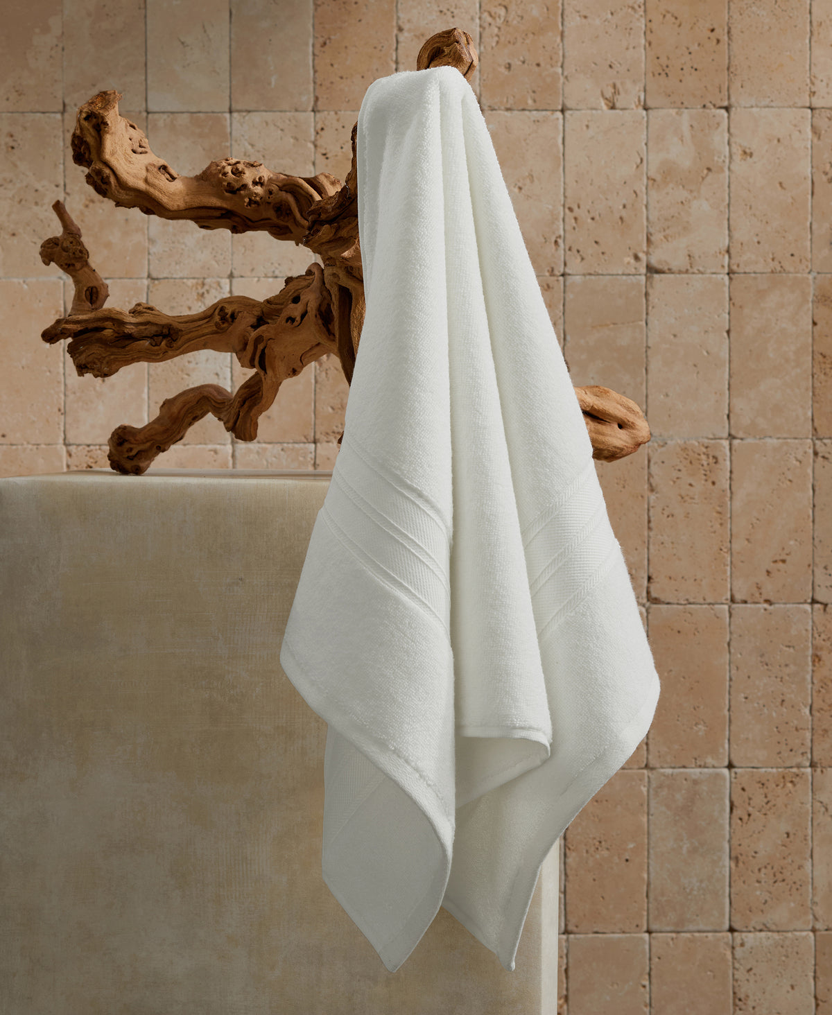 White towels hanging on natural driftwood towel rack against beige stone tile wall in modern bathroom