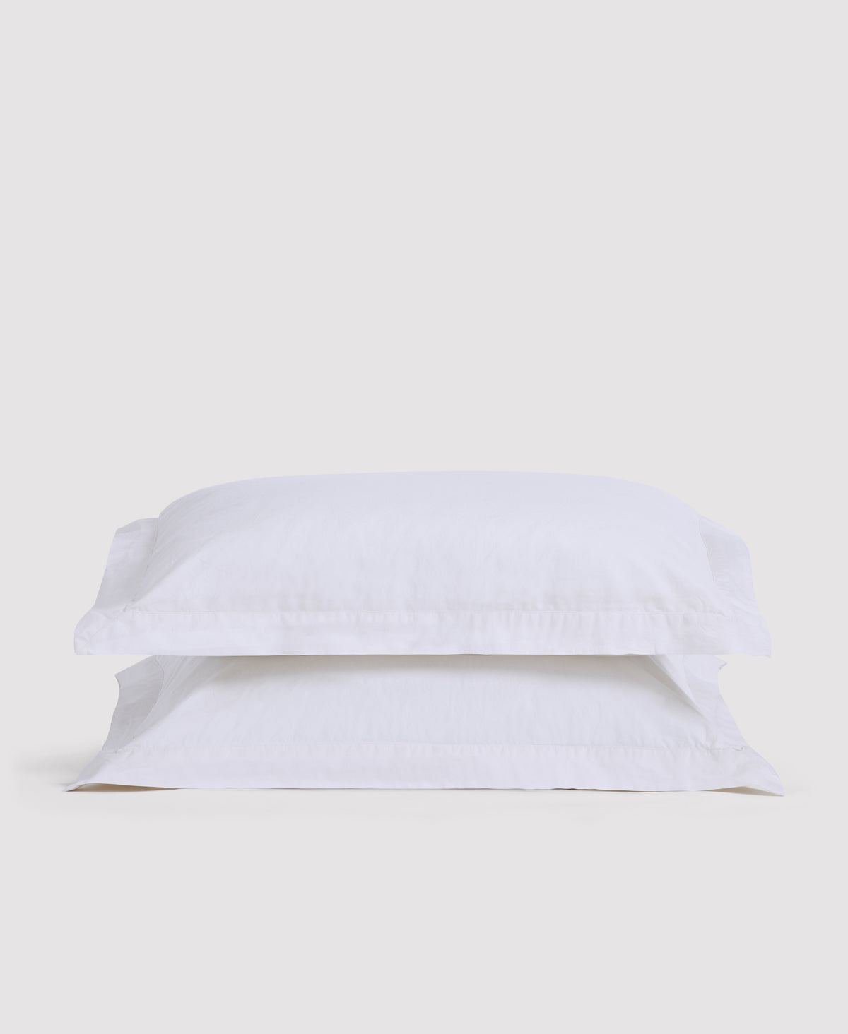 Two white pillowcases stacked on white bedding against a light gray background