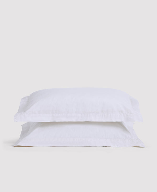 Two white pillowcases stacked on white bedding against a light gray background