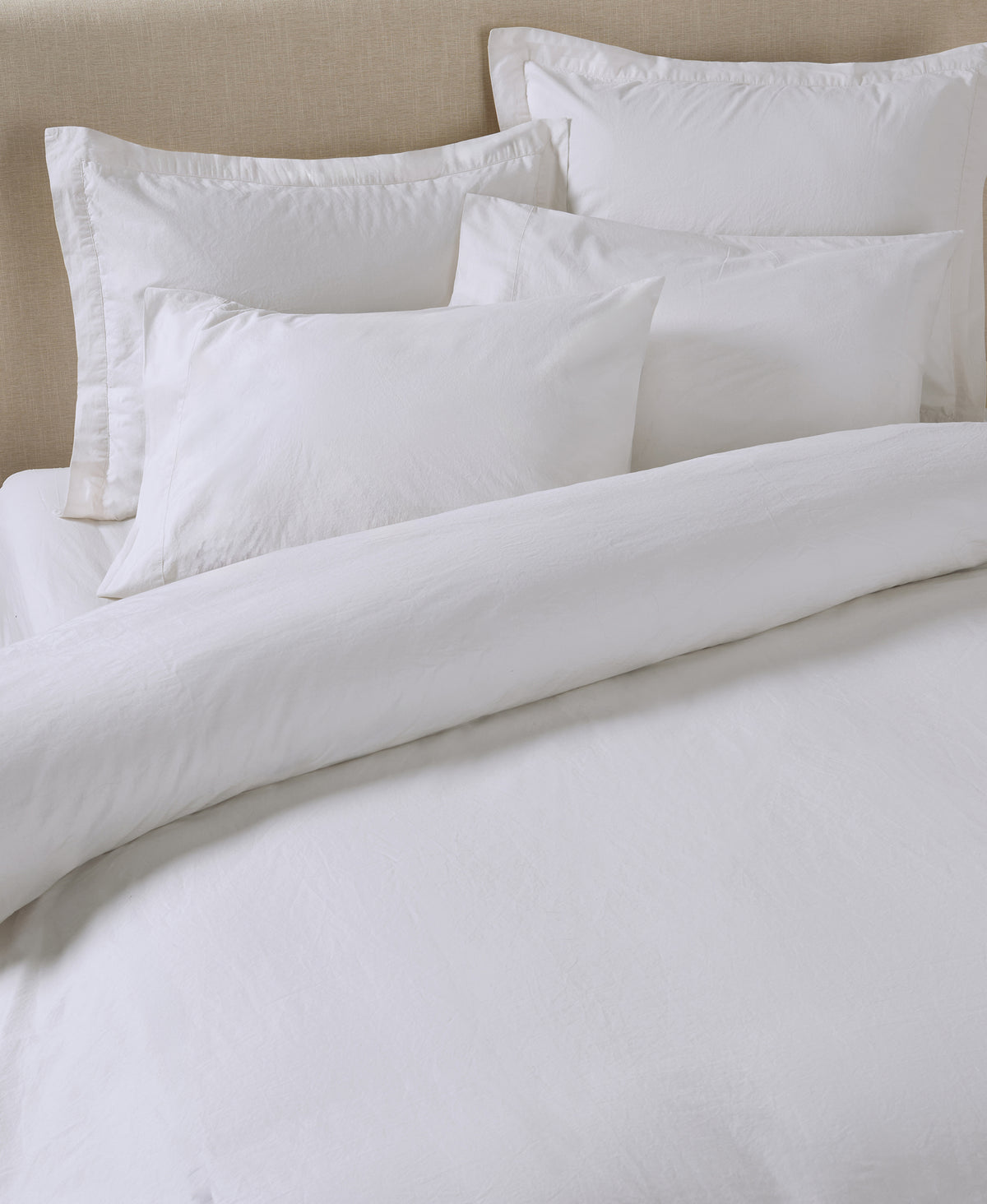 White bedding set with pillows and duvet on neutral upholstered headboard bed