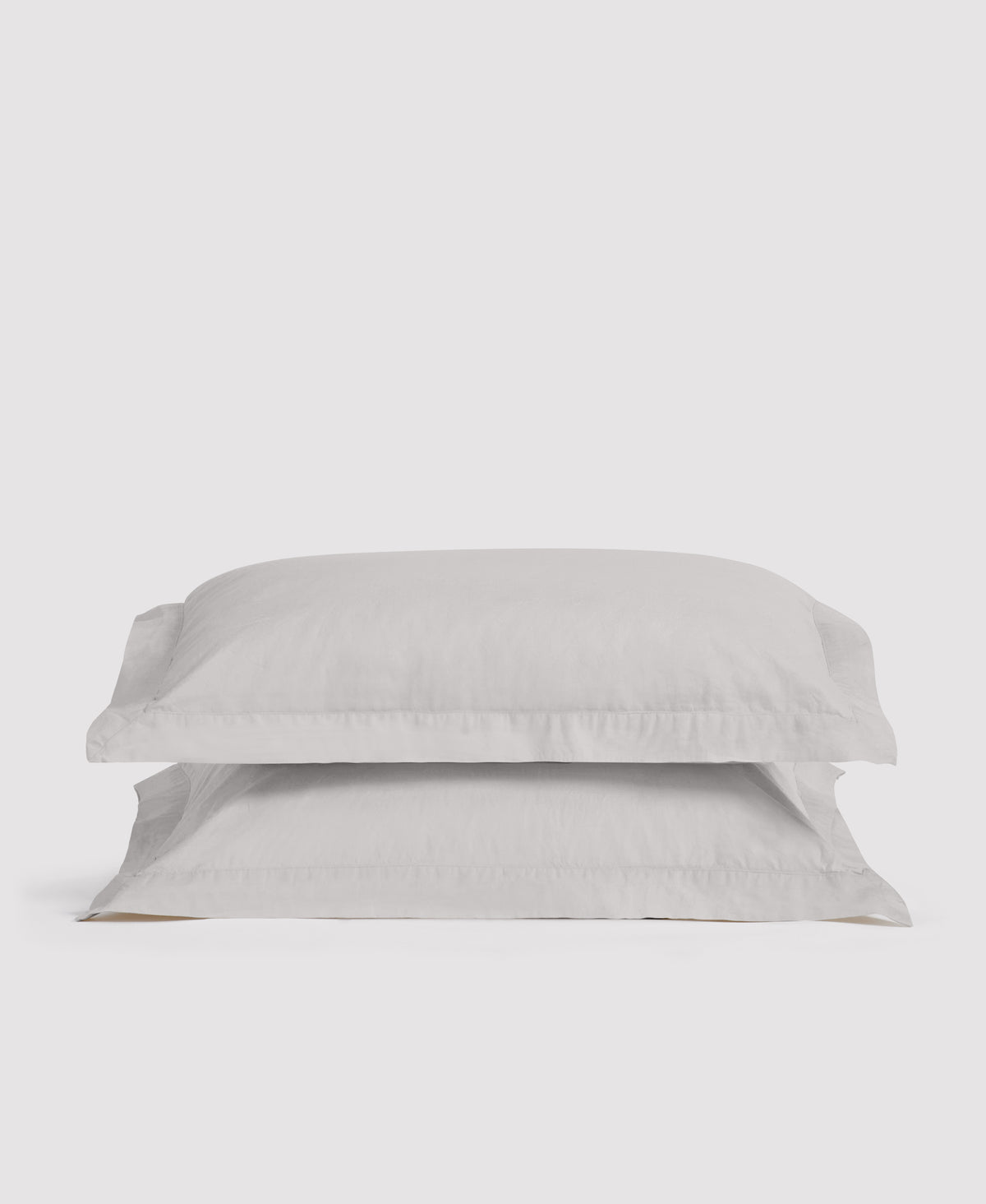 Two stacked white linen pillowcases with ruffled edges against a light gray background