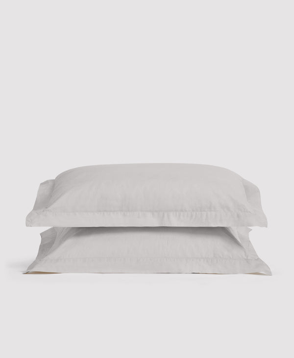 Two stacked white linen pillowcases with ruffled edges against a light gray background