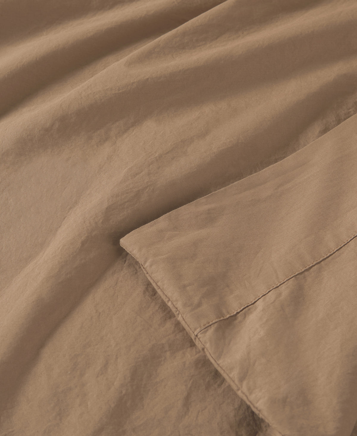Soft beige fabric draped in flowing folds with visible stitched seams and smooth texture