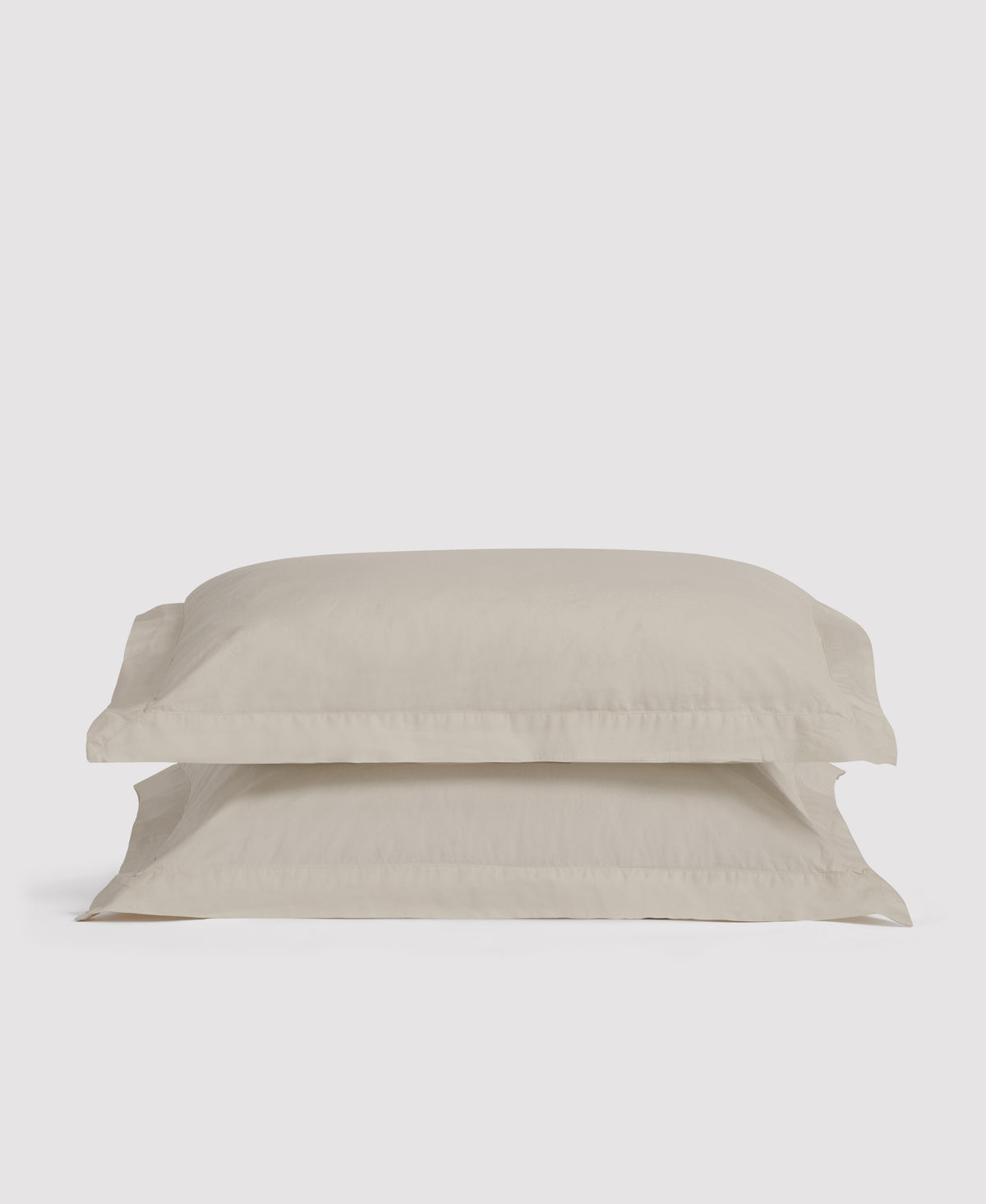 Two stacked beige linen pillowcases with decorative borders against a light gray background