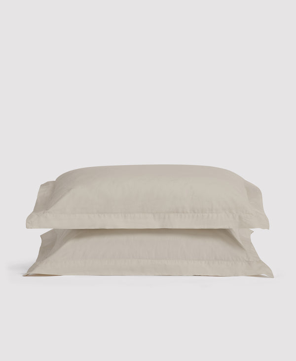 Two stacked beige linen pillowcases with decorative borders against a light gray background