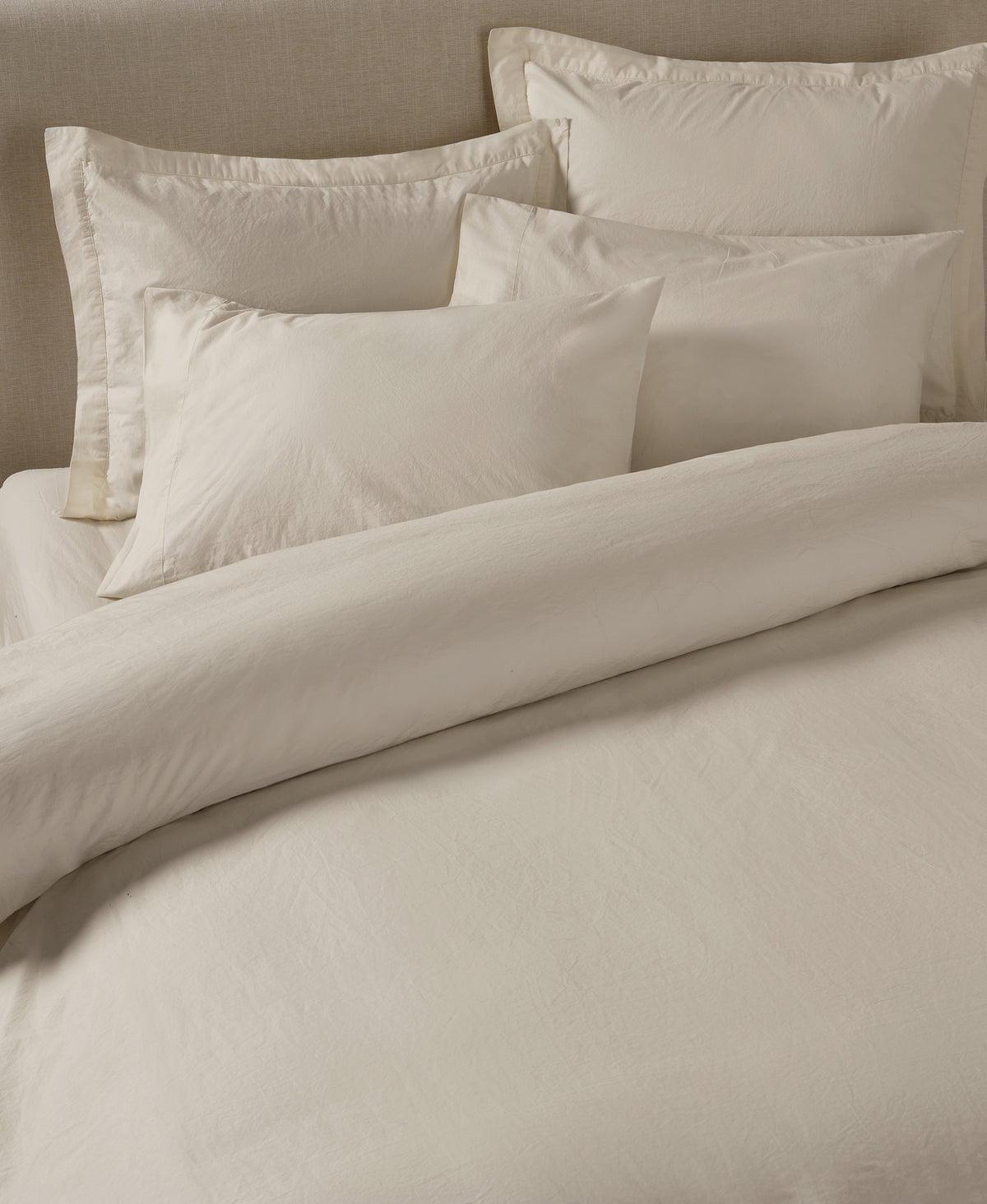 Neutral beige linen bedding set with pillows and duvet cover arranged on bed against matching headboard