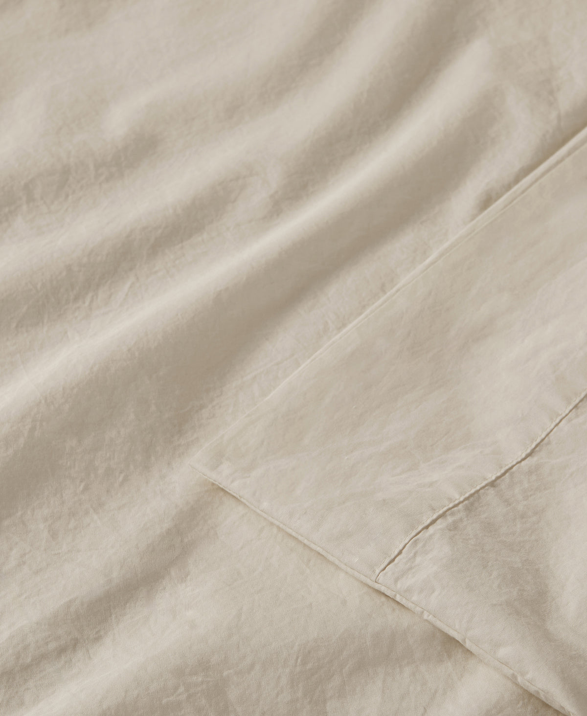 Close-up of cream-colored linen fabric with visible texture and hemmed edges, showing soft natural folds and weave detail.
