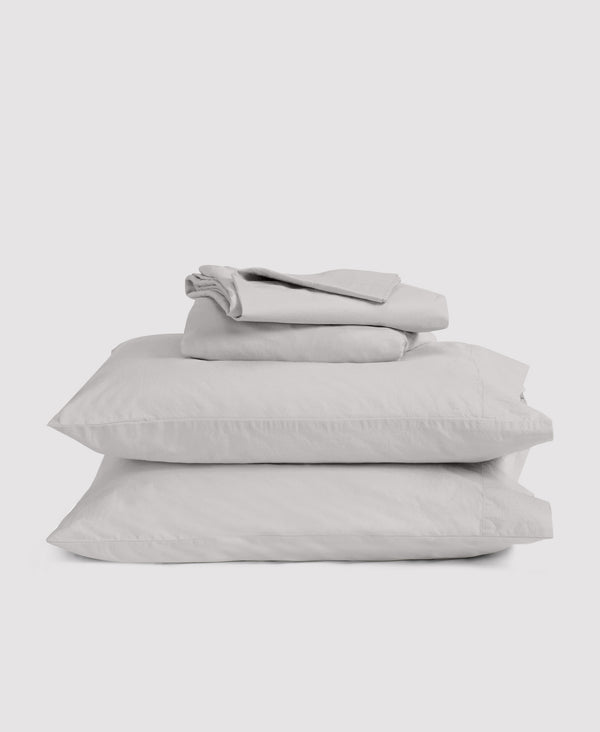 Stack of light gray linen bedding set including pillowcases and sheets folded neatly on white background