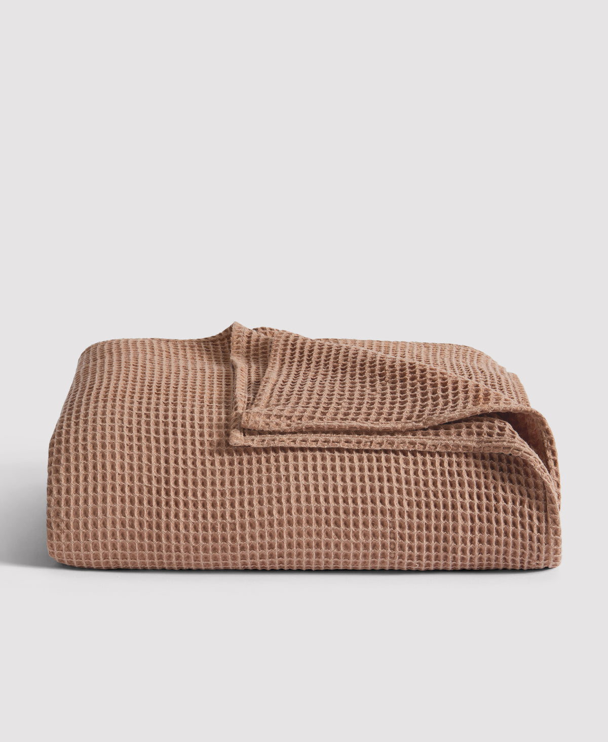 Folded waffle-textured blanket in warm terracotta brown color against light gray background