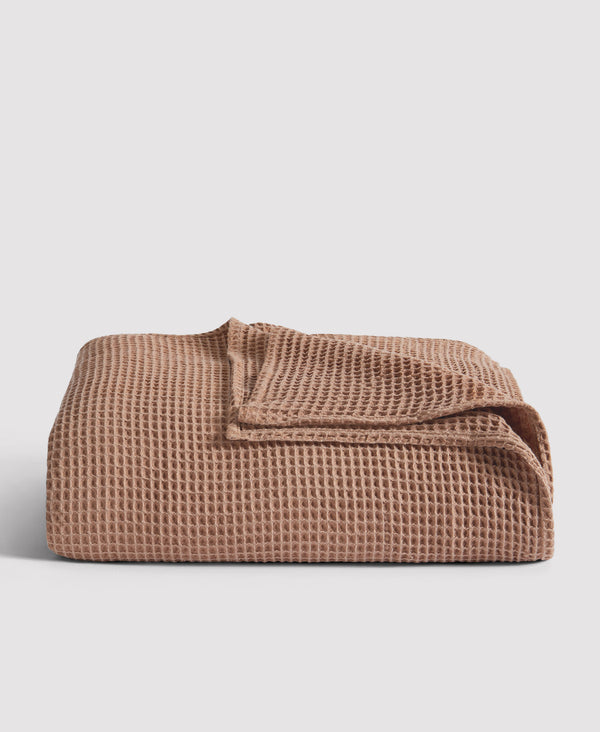 Folded waffle-textured blanket in warm terracotta brown color against light gray background
