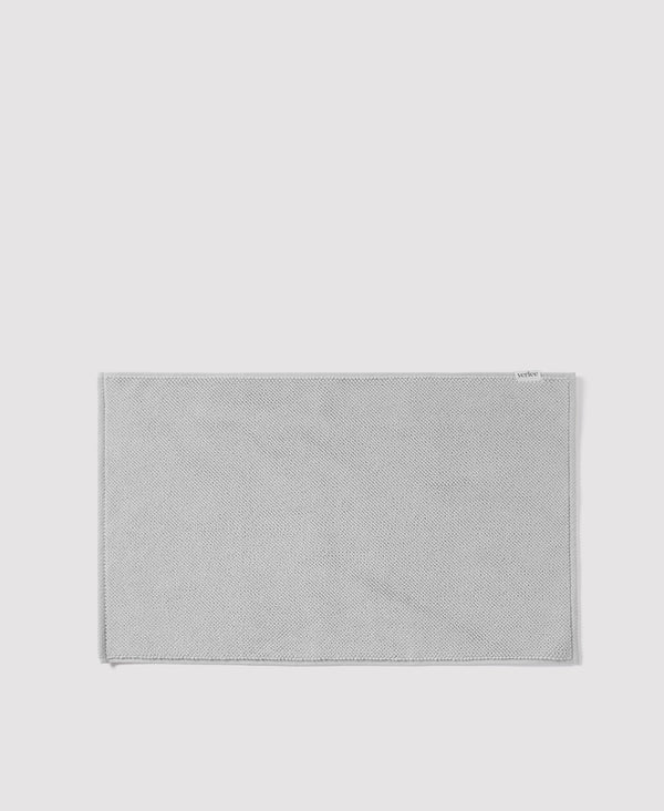 Gray woven textile bath mat or rug with herringbone pattern and bordered edges on white background
