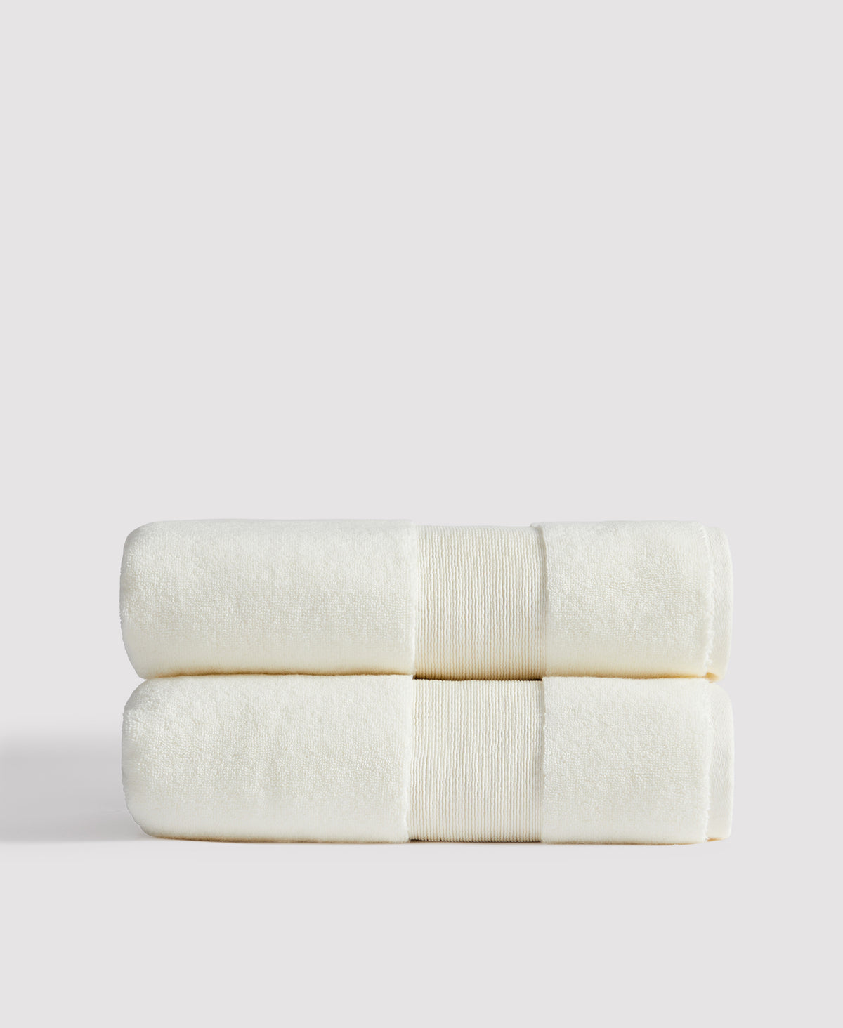 Two neatly folded cream-colored towels with decorative bands stacked on white surface against light gray background