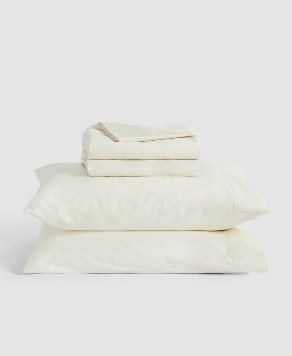 Neatly folded beige linen bedding set with duvet cover, two pillows, and flat sheet stacked on neutral background