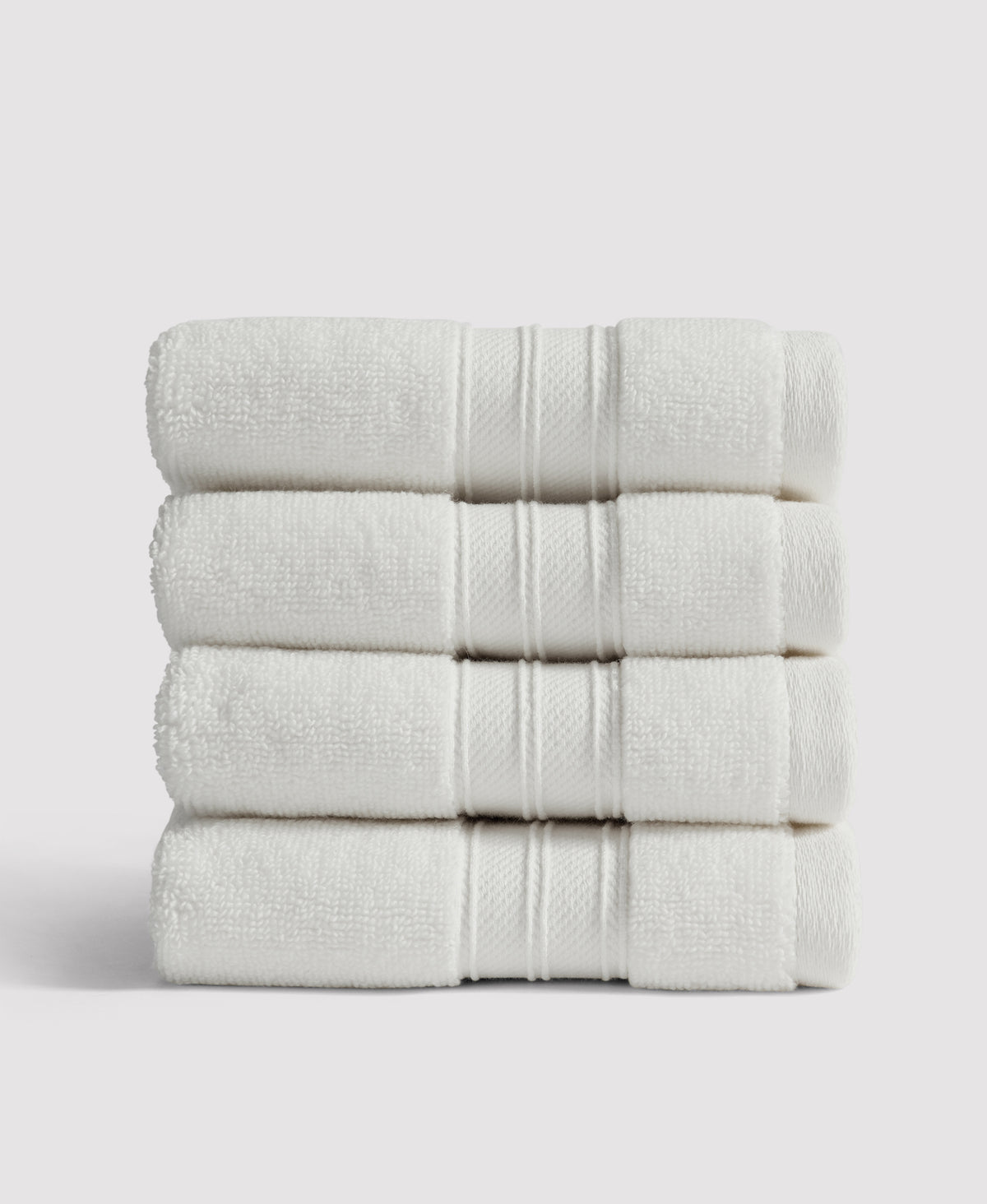 Stack of four neatly folded white bath towels with decorative border stripes against a light gray background