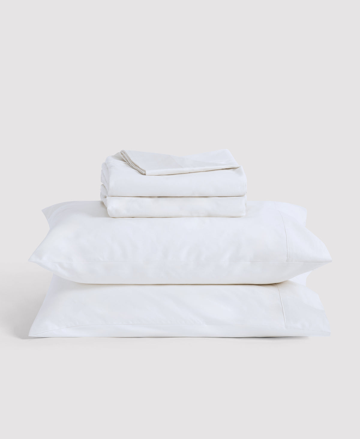Stack of cream-colored bedding with black stripe details including folded sheets and two pillows against white background