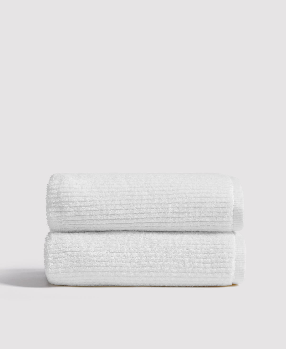 Two neatly stacked white ribbed towels on a white shelf against a neutral background
