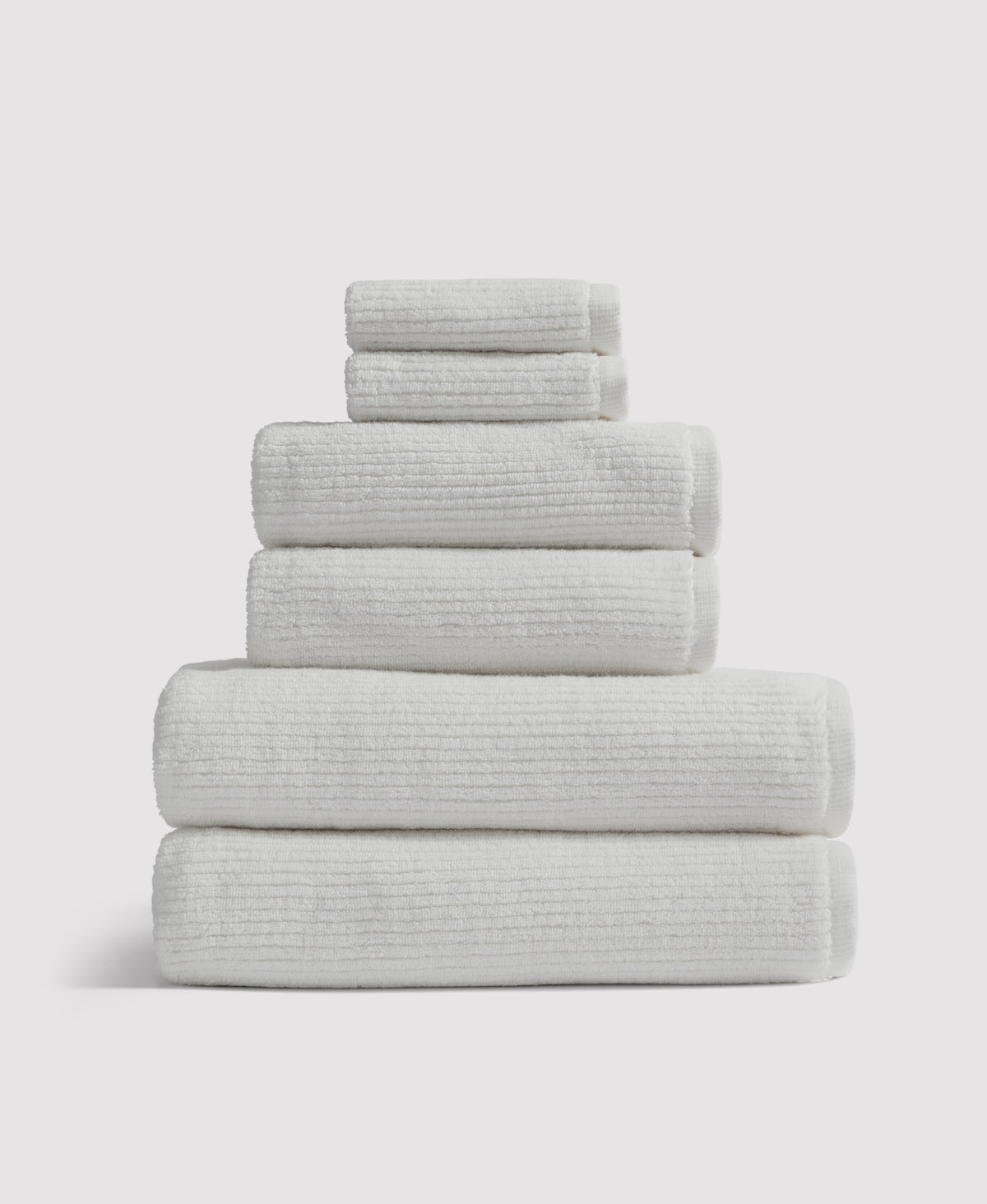 Stack of six neatly folded white textured towels arranged by size on white background