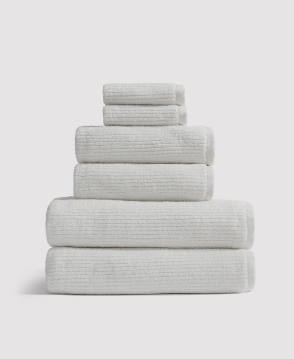 Stack of six neatly folded white textured towels arranged by size on white background