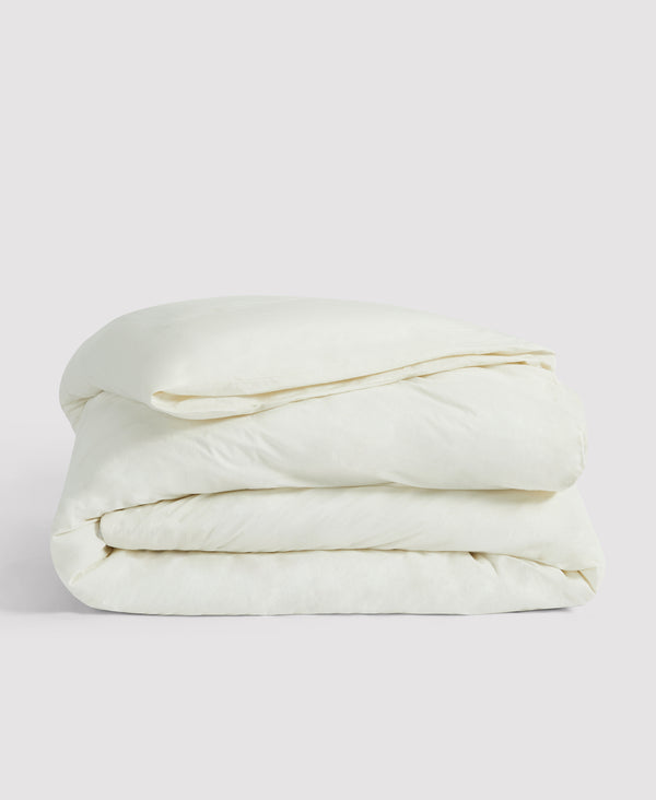 Neatly folded white or cream-colored bedding, likely a duvet or comforter, stacked against a light gray background.