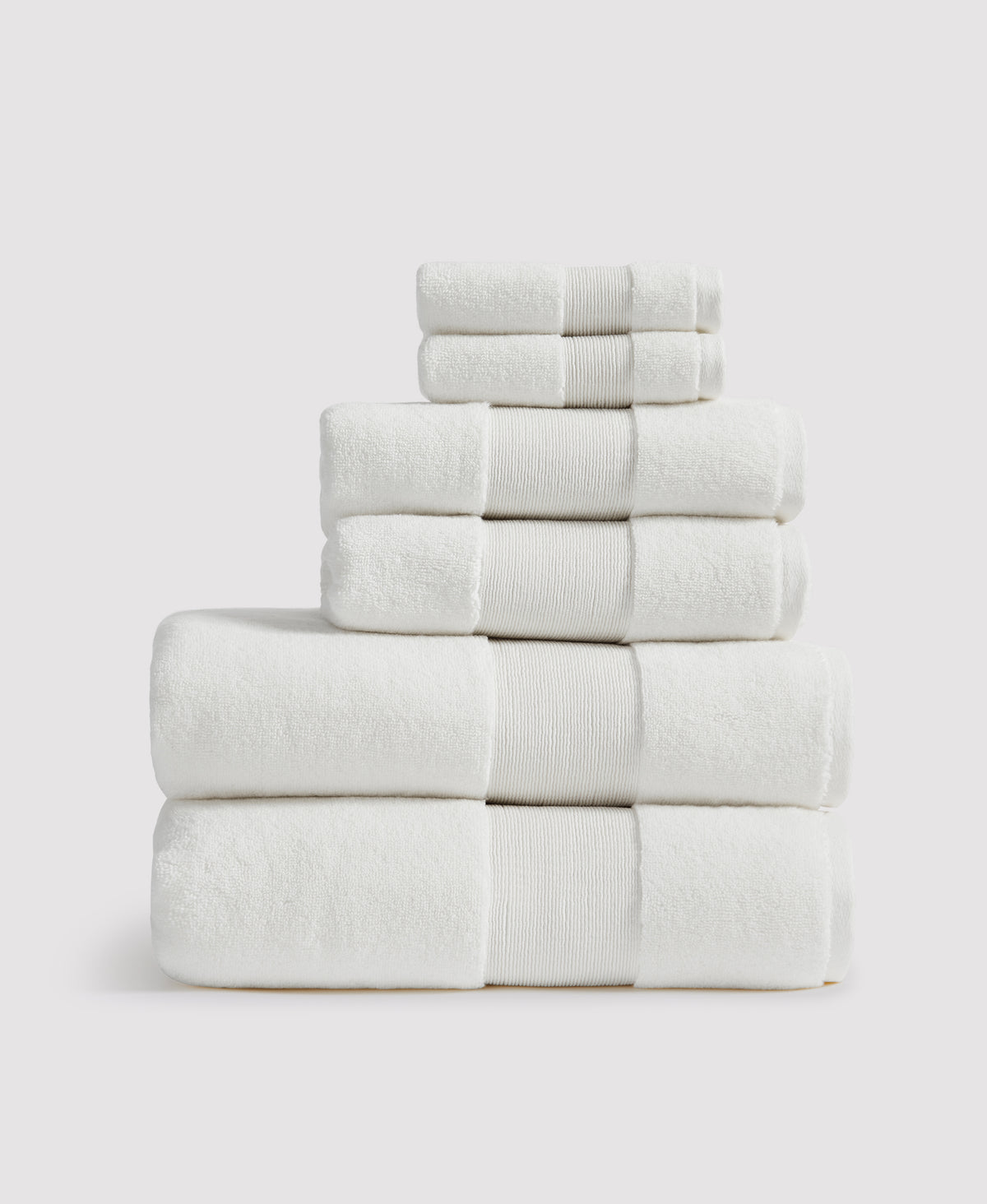 Stack of six neatly folded white towels with ribbed borders arranged by size from largest at bottom to smallest at top