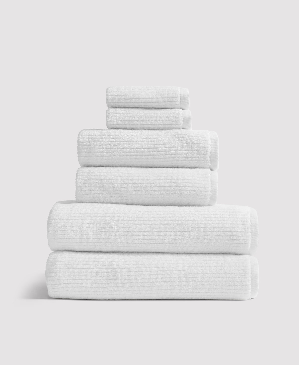 Stack of six white textured towels neatly folded and arranged by size from largest to smallest against white background