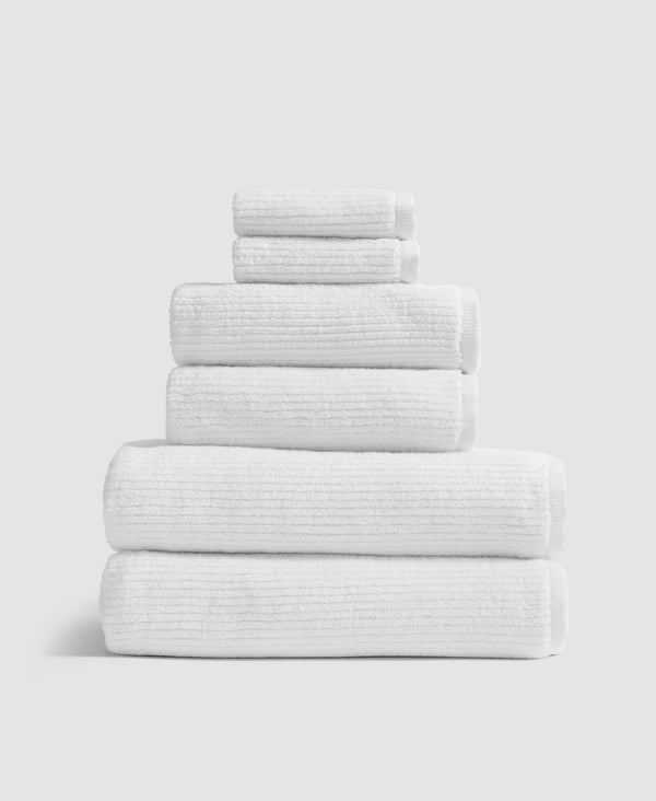 Stack of six white textured towels neatly folded and arranged by size from largest to smallest against white background