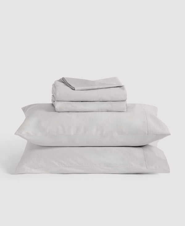 Stack of cream-colored bedding with black stripe details including folded sheets and two pillows against white background