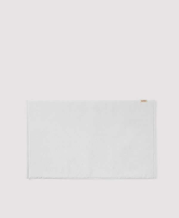 Light gray textured placemat or table mat with subtle woven pattern and small brown label in corner
