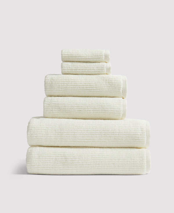 Stack of six neatly folded cream-colored towels arranged in descending size order against a white background