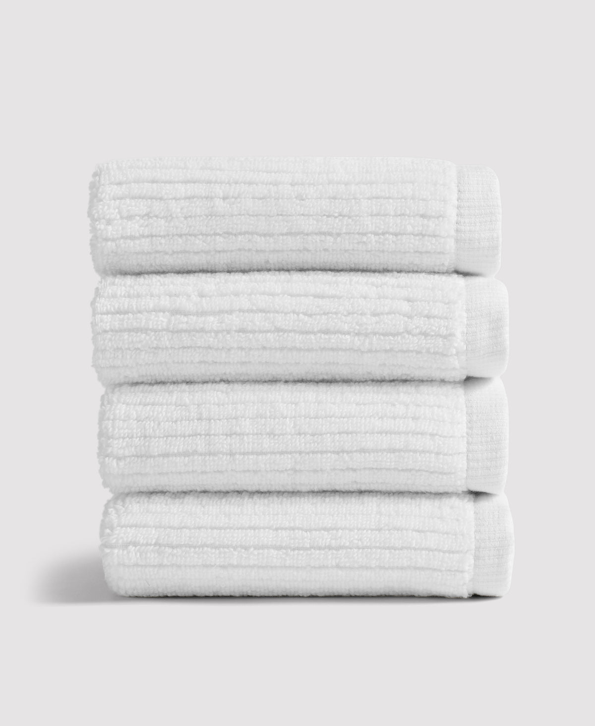 Stack of four neatly folded white textured towels against a light gray background