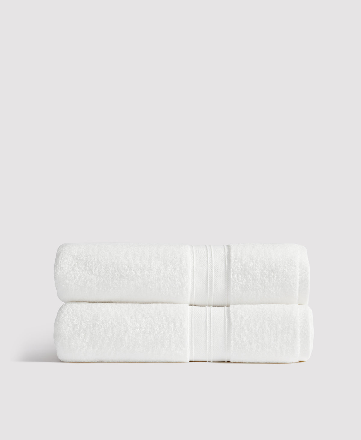Two neatly folded white towels with decorative stripe borders stacked on a white surface against a light gray background.