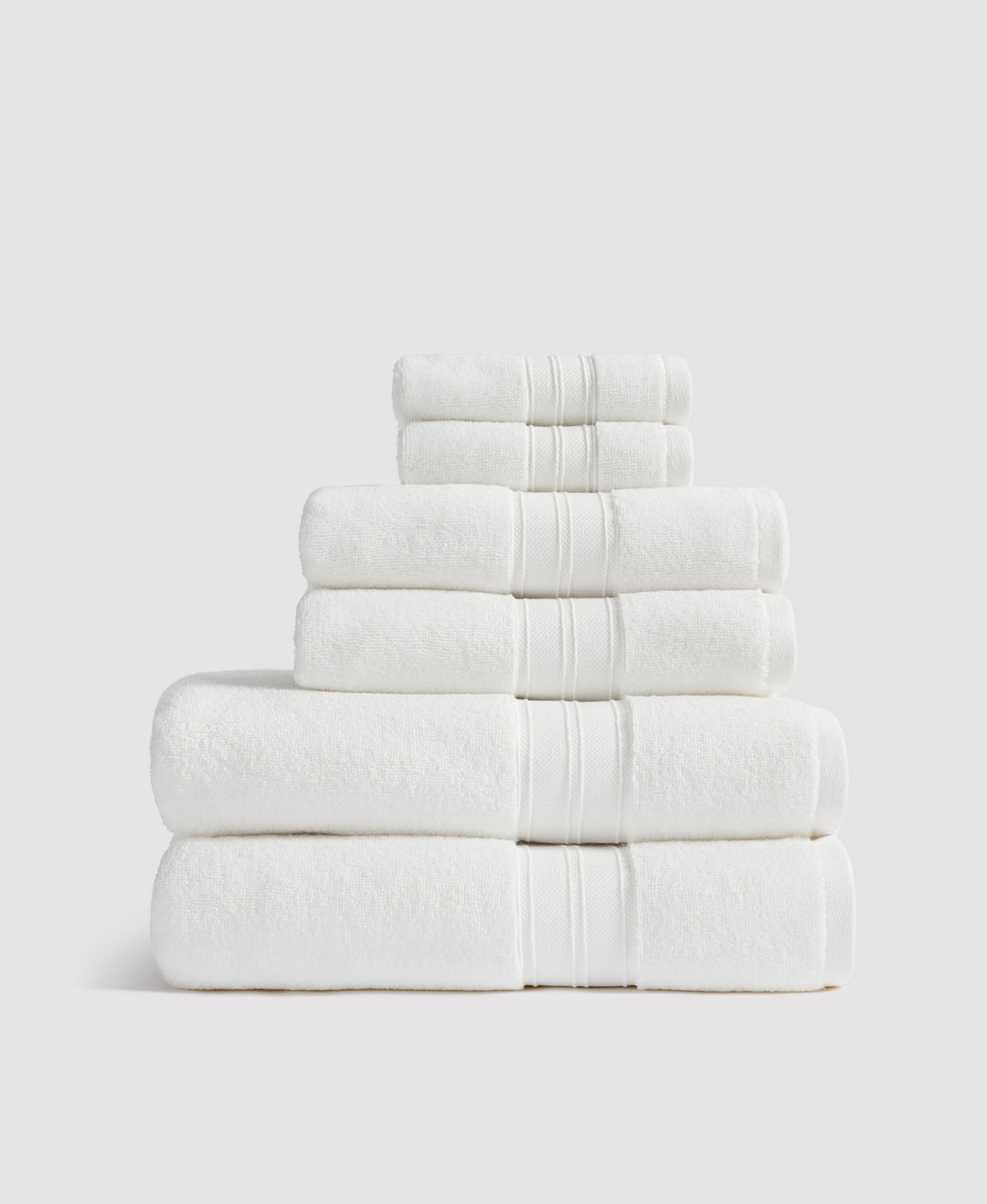 Stack of neatly folded white towels with decorative striped borders arranged from largest to smallest against a light gray background.
