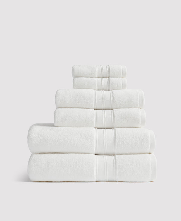 Stack of neatly folded white towels with decorative striped borders arranged from largest to smallest against a light gray background.