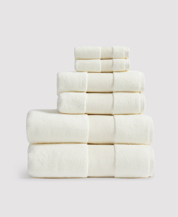 Stack of six neatly folded cream-colored towels with decorative borders arranged in a pyramid against white background