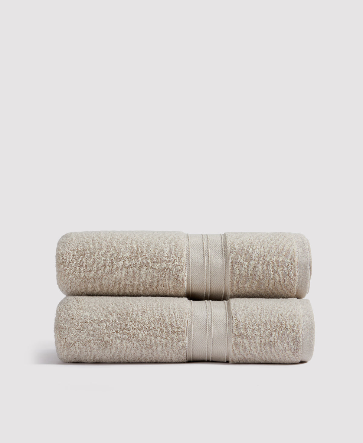 Two neatly stacked beige terry cloth bath towels with decorative border stripes on white background