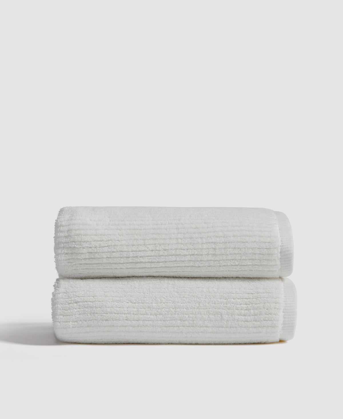 Two white ribbed towels neatly folded and stacked on a white surface against a light gray background.